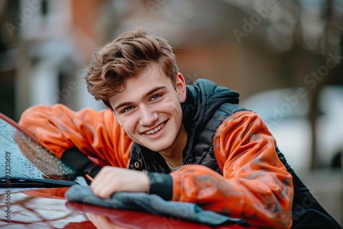 Teen boy smiling while washing a red car