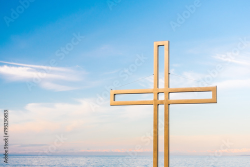 Golden cross against a background of blue sky with clouds. A minimalistic view of a gold-colored cross against the sky.