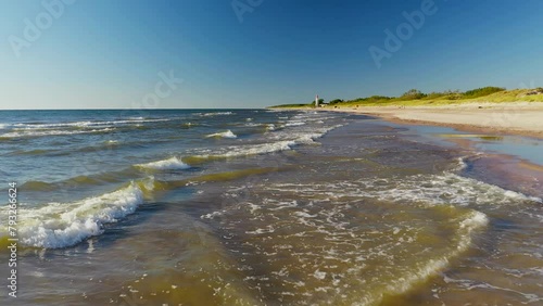 The sea coastline with beautiful rolling waves and a red lighthouse in the distance
