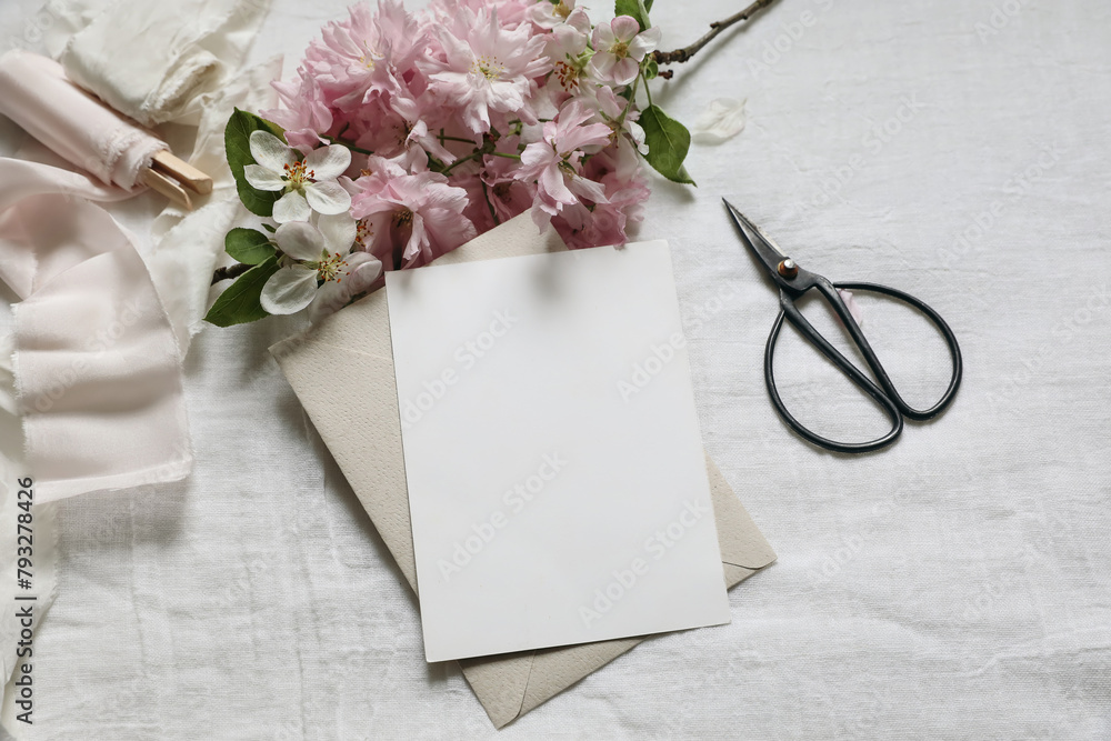 Wedding spring styled photo. Feminine scene mockup with pink blossoming Japanese cherry, apple tree branch. Blank paper greeting card, black scissors, white linen table background. Flat lay, top view. - obrazy, fototapety, plakaty 