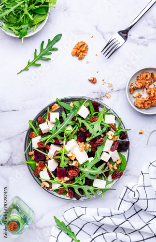 Beetroot and white cheese salad with arugula, lettuce, chard and walnuts, white table, copy space. Fresh useful vegetarian dish for healthy eating