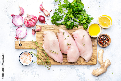 Raw chicken breast fillet on wooden cutting board, white table background, top view