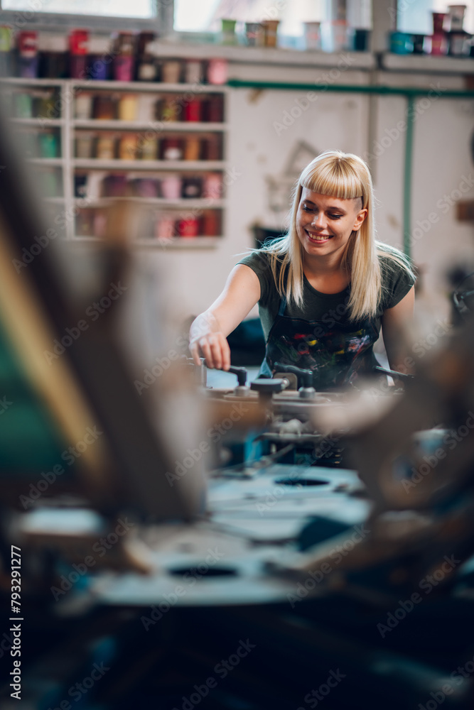 Smiling female graphic worker adjusting screen printing press at factory Smiling female graphic worker adjusting screen printing press at factory