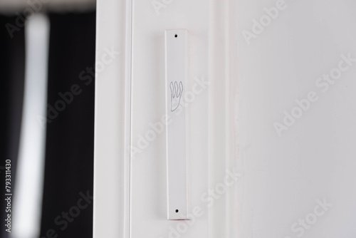 Hand gently touches the Jewish mezuzah on the doorpost, a prayer for home protection in Judaism. White interior, stylish modern mezuzah in Israel. photo