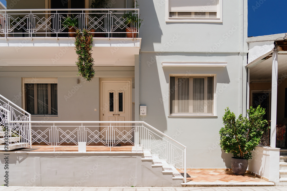 A clean and contemporary house facade featuring a white railing balcony, decorative plants, and a welcoming entrance.