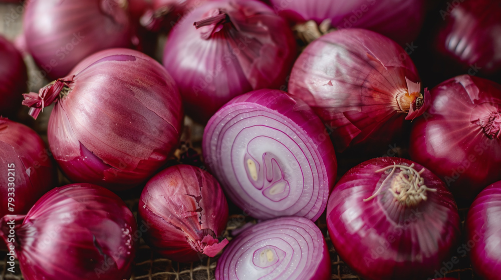 Red onions, one sliced in the middle with a white center, lying on top of other whole onions. A close up top view shot. 