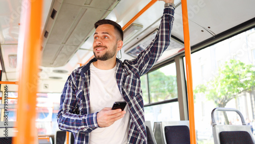 Young man riding in a bus and sending message on smartphone