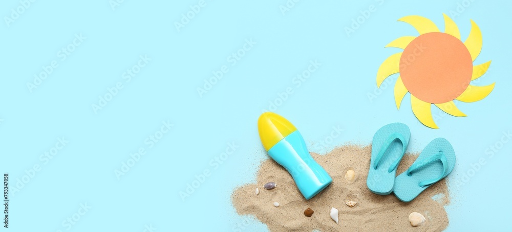 Bottle of sunscreen cream, flip-flops, paper sun and sand on light blue background with space for text