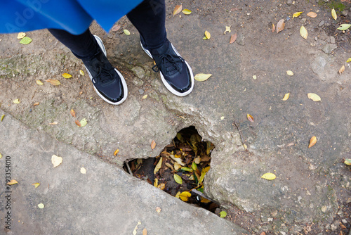 A person is standing on a sidewalk with a hole in the ground