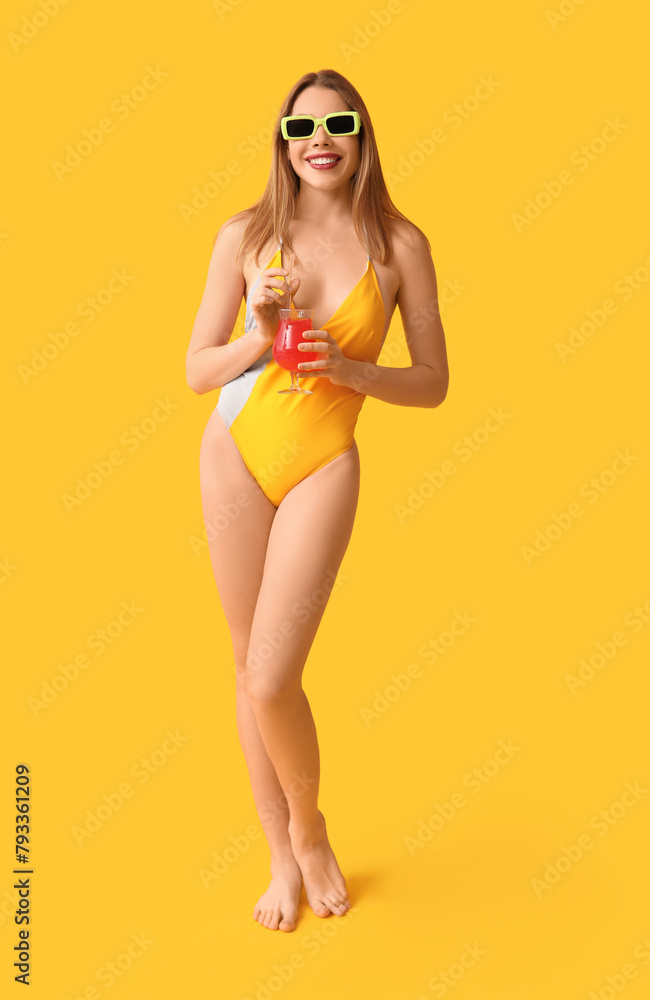 Pretty young woman in tank swimsuit and with cocktail on yellow background Pretty young woman in tank swimsuit and with cocktail on yellow background