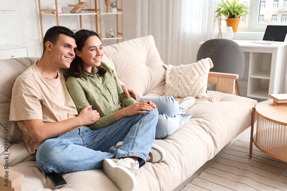 Young couple watching TV on sofa at home