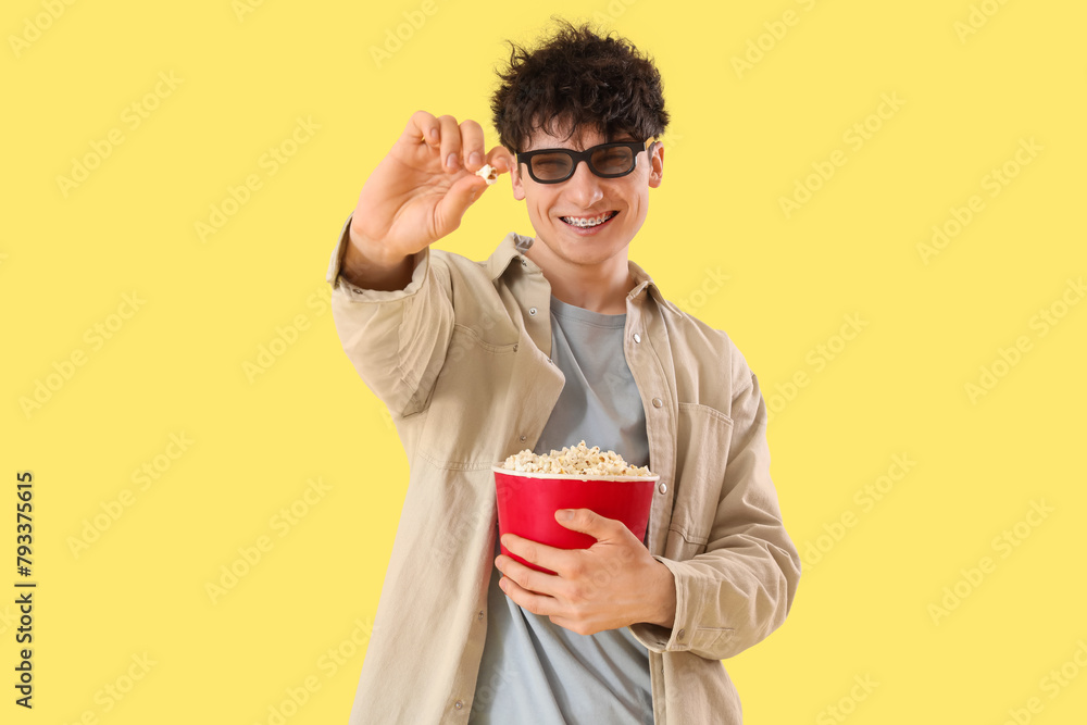 Young man in 3d eyeglasses showing popcorn on yellow background Young man in 3d eyeglasses showing popcorn on yellow background