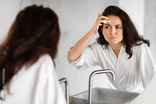 Worried woman checking wrinkles in mirror in bathroom photo