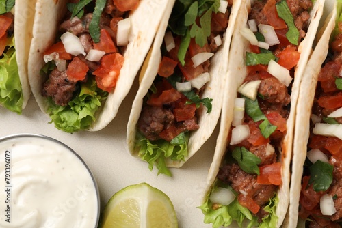 Delicious meat tacos with vegetables, lime and sauce on light table, flat lay