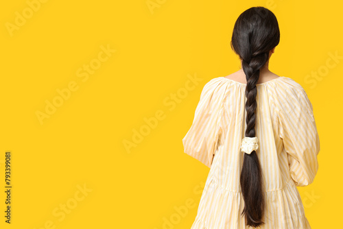 Woman with pigtail and silk scrunchy on yellow background, back view photo