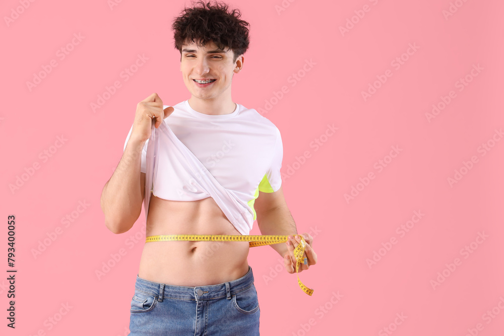 Handsome young happy sporty man with measuring tape on pink background. Weight loss concept Handsome young happy sporty man with measuring tape on pink background. Weight loss concept