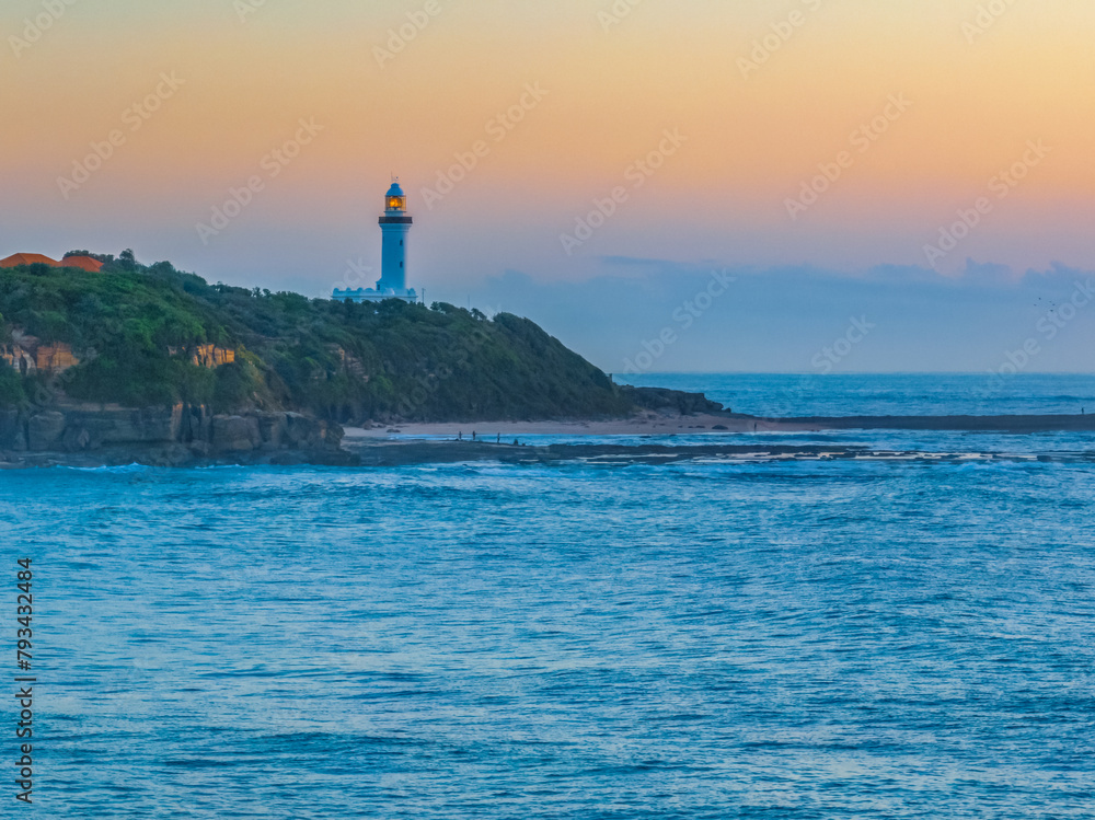Sunrise over the sea and rocks with clear skies and lighthouse