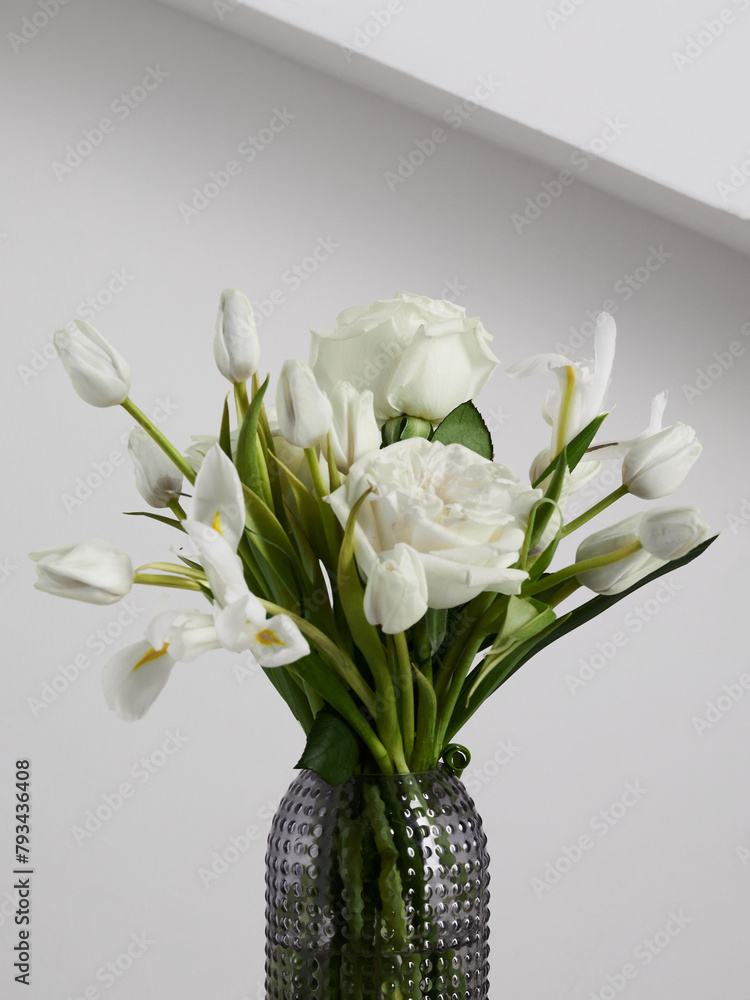 White flowers in a transparent ribbed vase, against a white wall background