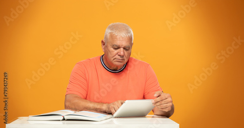 elderly man at a table with a tablet and a book
