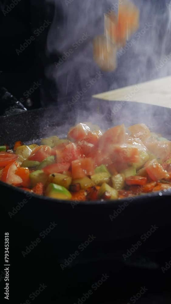 cook adds red, juicy tomato slices to a frying pan where colorful vegetables are already cooking. Vertical. Close up. 4k. cook adds red, juicy tomato slices to a frying pan where colorful vegetables are already cooking. Vertical. Close up. 4k.