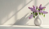  lilac flowers in a white vase on a table, against a white wall background, with natural light