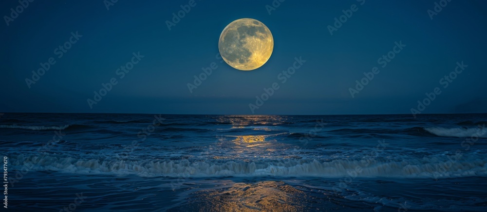 Full moon ascending above the sea as powerful waves break on the shore in the foreground Full moon ascending above the sea as powerful waves break on the shore in the foreground