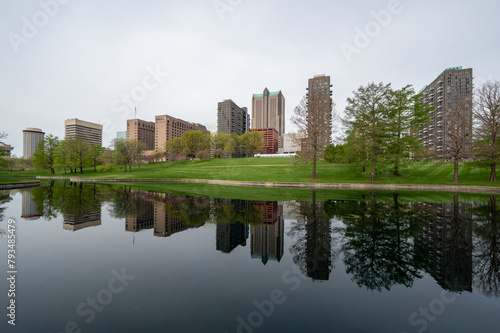 Buildings of city of St Louis, Missouri reflected in reflecting pool in Gateway Arch National Park on overcast April morning.