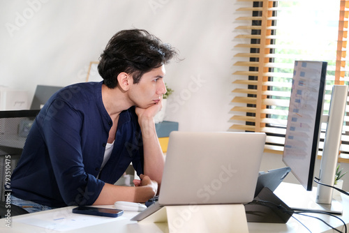 Young man thinking while working with computer at home office, wrok from home