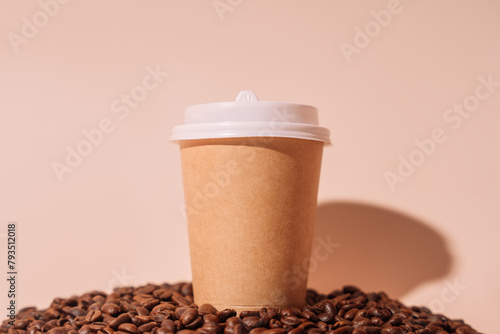 Paper cup with takeaway coffee on a pile of coffee beans against a beige background.