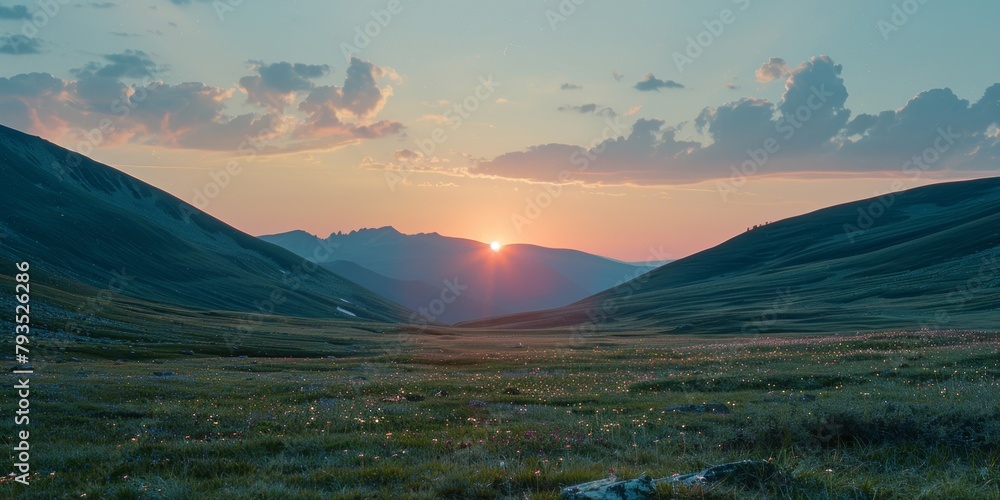 Sun setting behind mountains over a tranquil meadow with wildflowers.