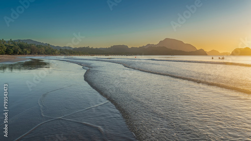 A calm sunset on a tropical island. The waves of the ocean roll towards the shore, spread over the beach. Reflection on the wet smooth sand.   The evening sky is highlighted in orange. Philippines. 