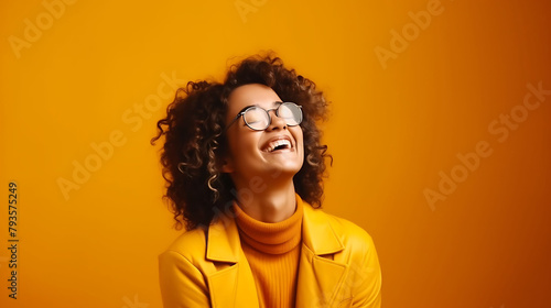 Happy woman wearing glasses  smiling warmly  arms crossed  against a bold mustard yellow backdrop  radiating joy