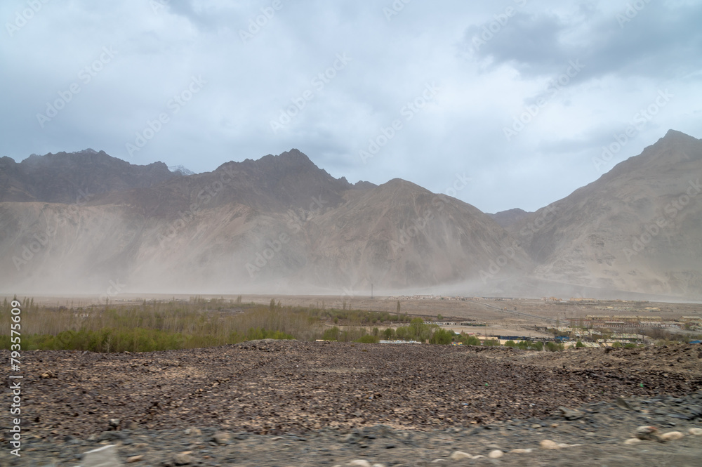 Rocky Terrains of Nubra Valley in Ladakh, India. Background of Himalayas and dramatic clouds. View of cars driving through the zig zag Himalayan roads. Rocky Terrains of Nubra Valley in Ladakh, India. Background of Himalayas and dramatic clouds. View of cars driving through the zig zag Himalayan roads.