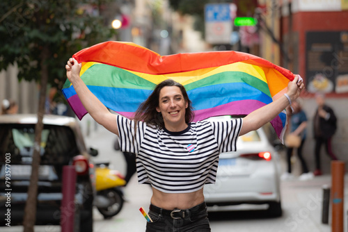 Portrait of a happy transgender girl waving a rainbow flag in a city street. LGBTQ+ community and diversity concept