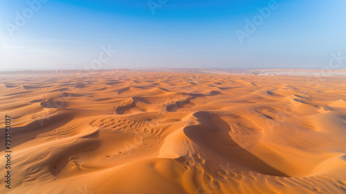 Aerial view of a vast desert with sand dunes rippling towards the horizon under a clear blue sky