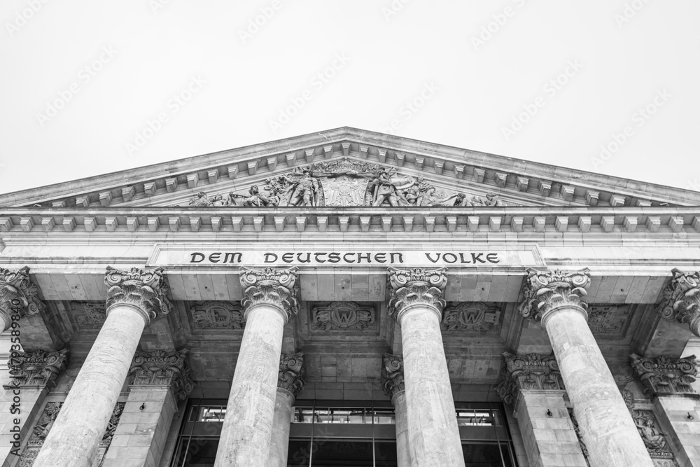Obraz premium The monochrome facade of the Reichstag building, showcasing its iconic pillars and inscription: Dem Deutschen Volke. The seat of the German Bundestag, Berlin, Germany.. Black and white image.