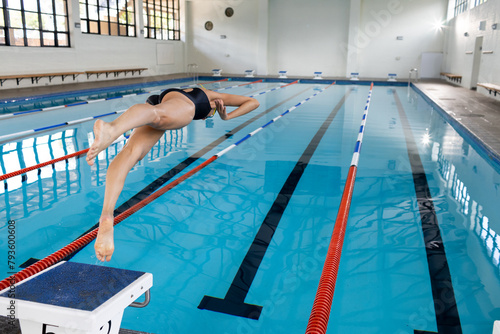 A biracial young female swimmer diving into indoor swimming pool, copy space