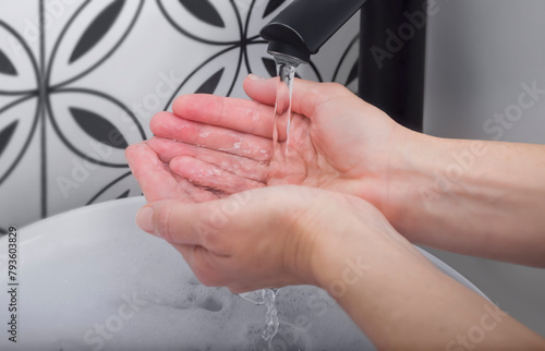 A stream of clean water flows from the tap into a woman's cupped hands. Close-up