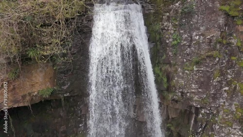 An slow motion aerial view of Melinclourt Waterfall on an overcast day, Neath Port Talbot, South Wales. Flying away from the top of the fall while tilting downwards photo