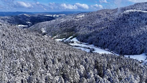 Drone slow fly in the Meurthe valley in Plainfaing with snow covered landscape during springtime with blue sky and big clouds photo