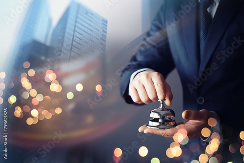 Man in a suit holding metal service bell on black background, double exposure skyscraper concept reserve hotel, closeup