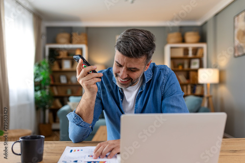Business professional having a phone call. Business man analyzing data using computer while talking on the phone in the office. Young grinning professional man in office.