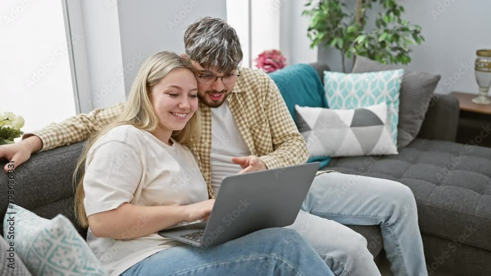 A happy couple relaxes at home on a couch using a laptop, suggesting comfort and togetherness in a modern living room setting. A happy couple relaxes at home on a couch using a laptop, suggesting comfort and togetherness in a modern living room setting.