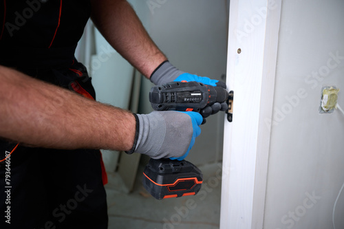 Construction worker with a screwdriver installing a door. Accessories for assembling, install furniture, repair home. Man dressed in work attire, helmet and protective glasses. Home renovation concept