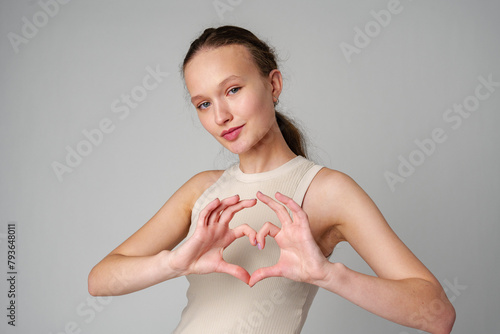 Young woman gesturing heart shape with hands on gray background