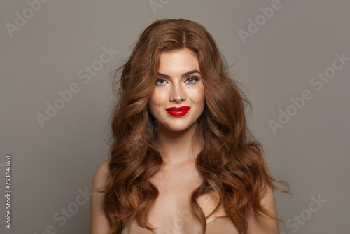 Young fashionable redhead woman with long wavy hair and make-up. Studio headshot portrait of fashion model lady with red colorful shine lipstick. Haircare, skin care and coloration concept