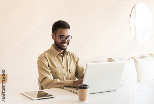 Young handsome man using laptop at home. Businessman or student working on computer online. Freelance, online marketing, education and technology concept
