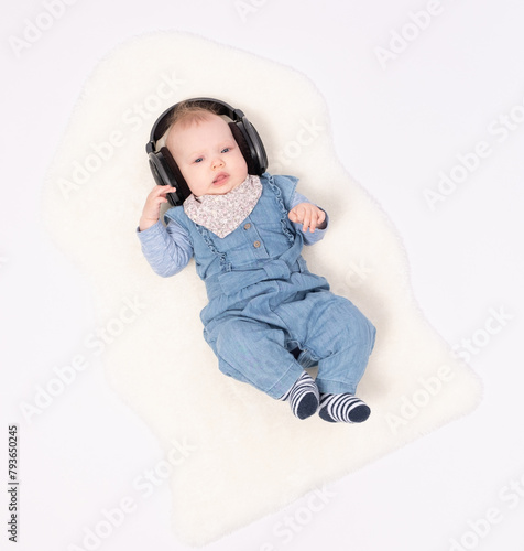 Charming baby girl is lying on the floor and hearing music wearing in headphones