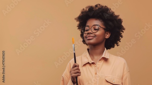 Artistic Flair: Artistic African American teen holding a paintbrush, isolated on a simple beige background. With a playful smirk and a creative glow, styled as an inspirational creative portrait. photo