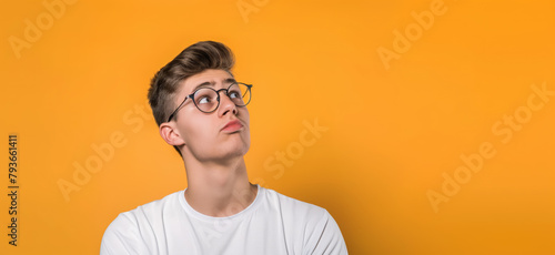 A young man wearing glasses looking upwards, thinking, on an orange background, concept of curiosity. Generative AI